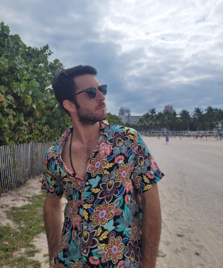 Model wearing a dark multicolor floral Unilome camp-collar shirt on the beach